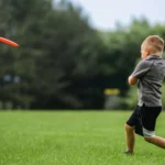 Niño jugando felizmente sobre césped Kikuyo, disponible en Rootedy, tu tienda de esquejes